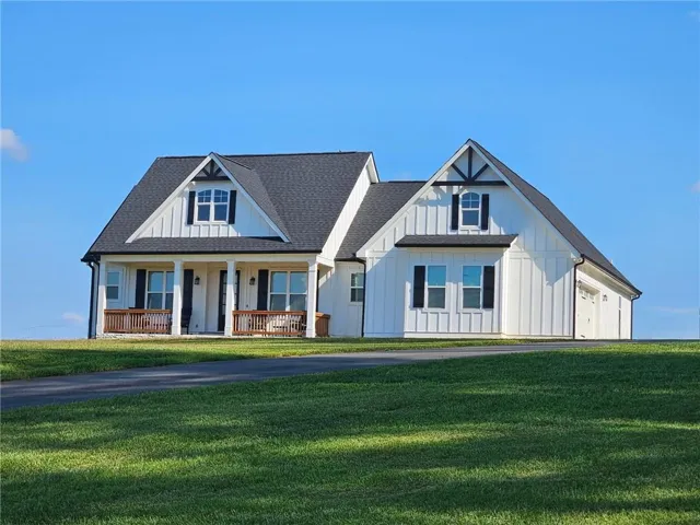 Modern farmhouse featuring covered porch, a front lawn, board and batten siding, and a shingled roof