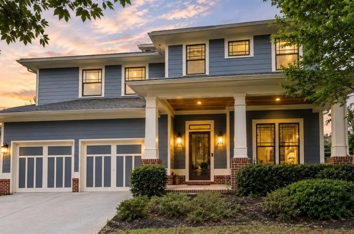 Two-story exterior with blue siding, brick accents, and a covered front porch featuring white columns