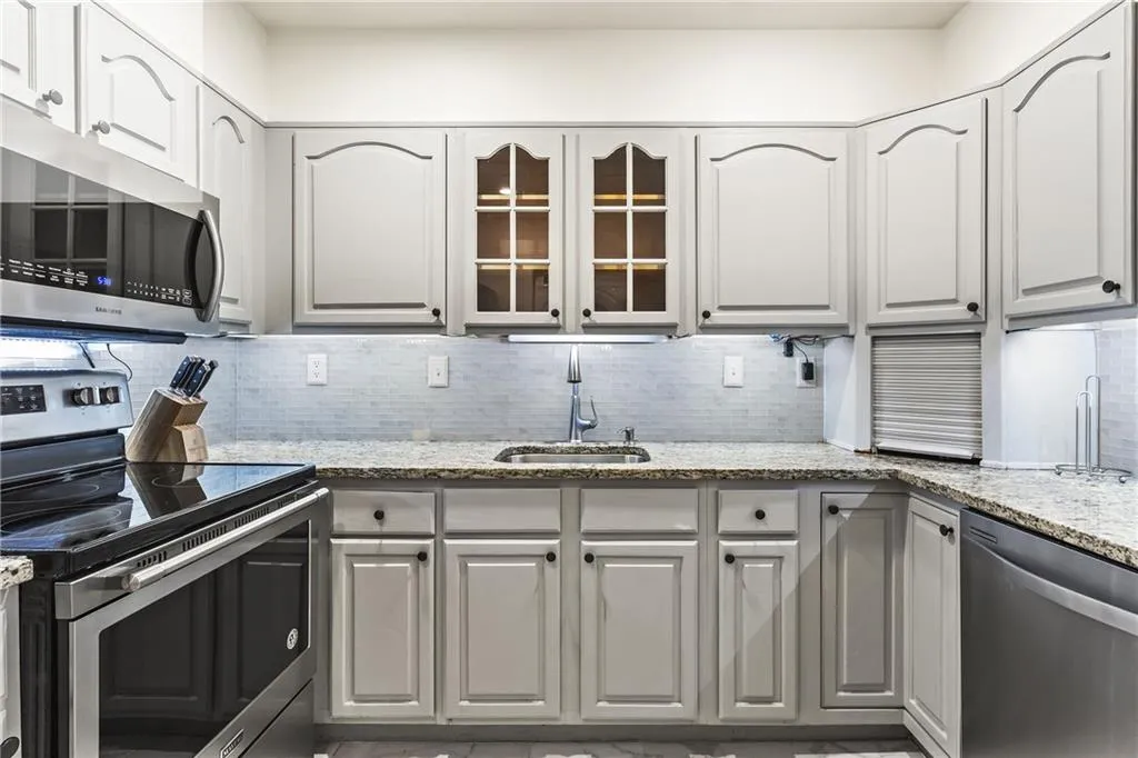 Kitchen featuring light-toned cabinetry with dark hardware, granite-style countertops, and a subway tile backsplash