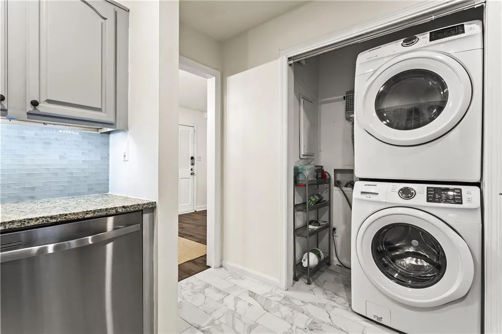 Convenient laundry area featuring a stacked washer and dryer, accompanied by a white marble-look floor