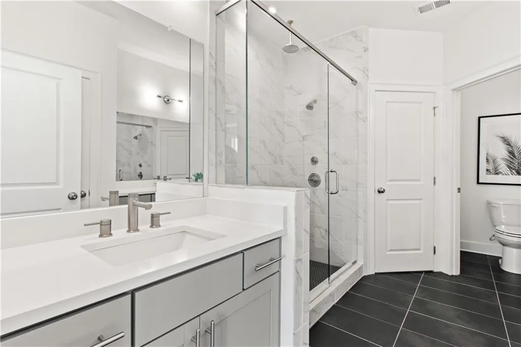 Bathroom with a marble finish shower, vanity, and dark tile patterned flooring