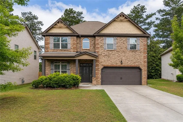 Brick and siding exterior featuring gabled rooflines, decorative window shutters, an arched entry window, an attached two-car garage, and a concrete driveway
