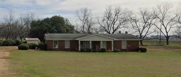 Brick exterior, covered porch entry, white columns, mature landscaping, and a detached storage shed