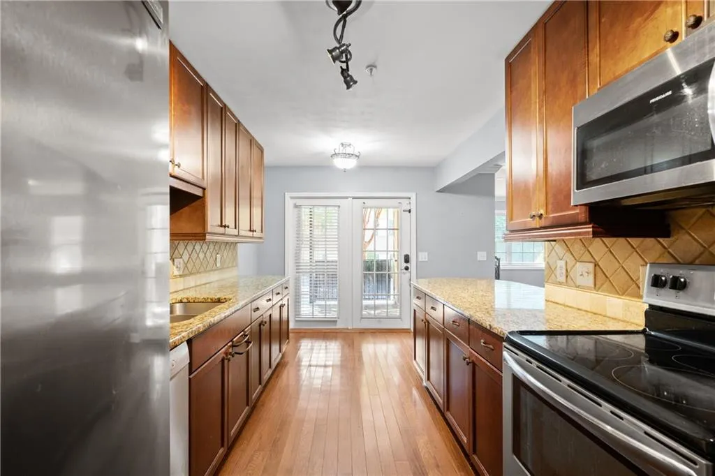 Kitchen featuring light wood-type flooring, light stone counters, stainless steel appliances, and decorative backsplash