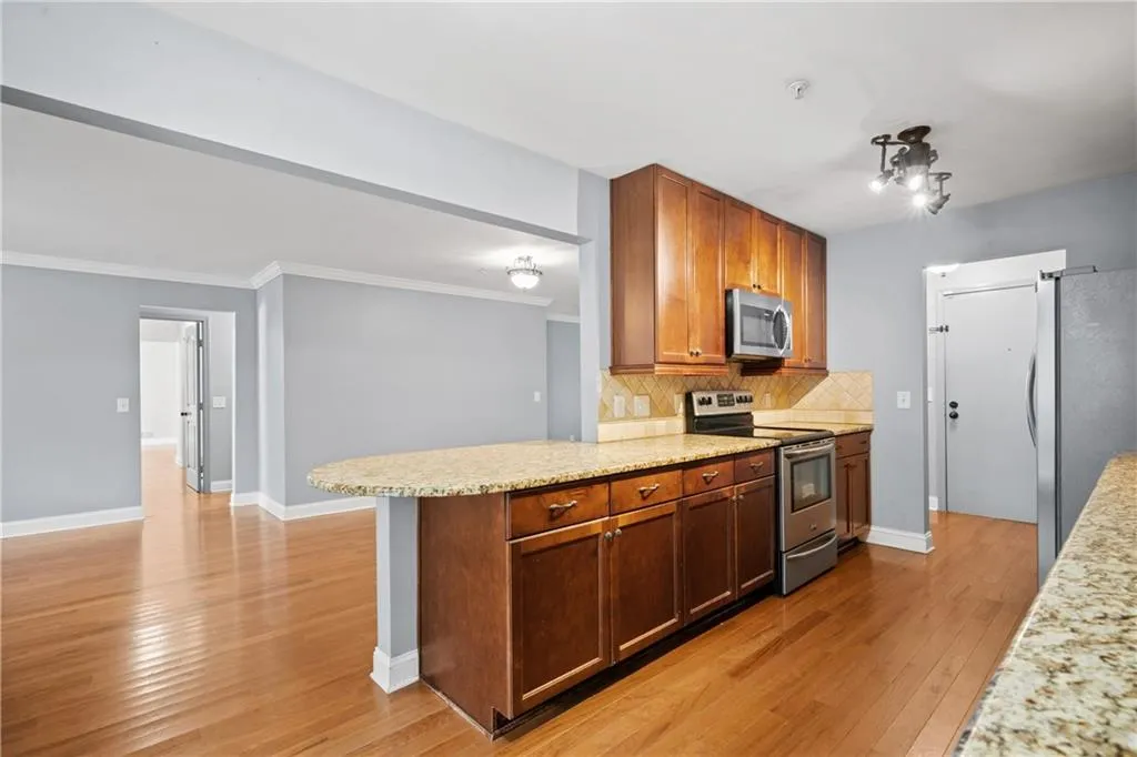 Kitchen featuring ornamental molding, backsplash, stainless steel appliances, light stone counters, and light hardwood / wood-style floors
