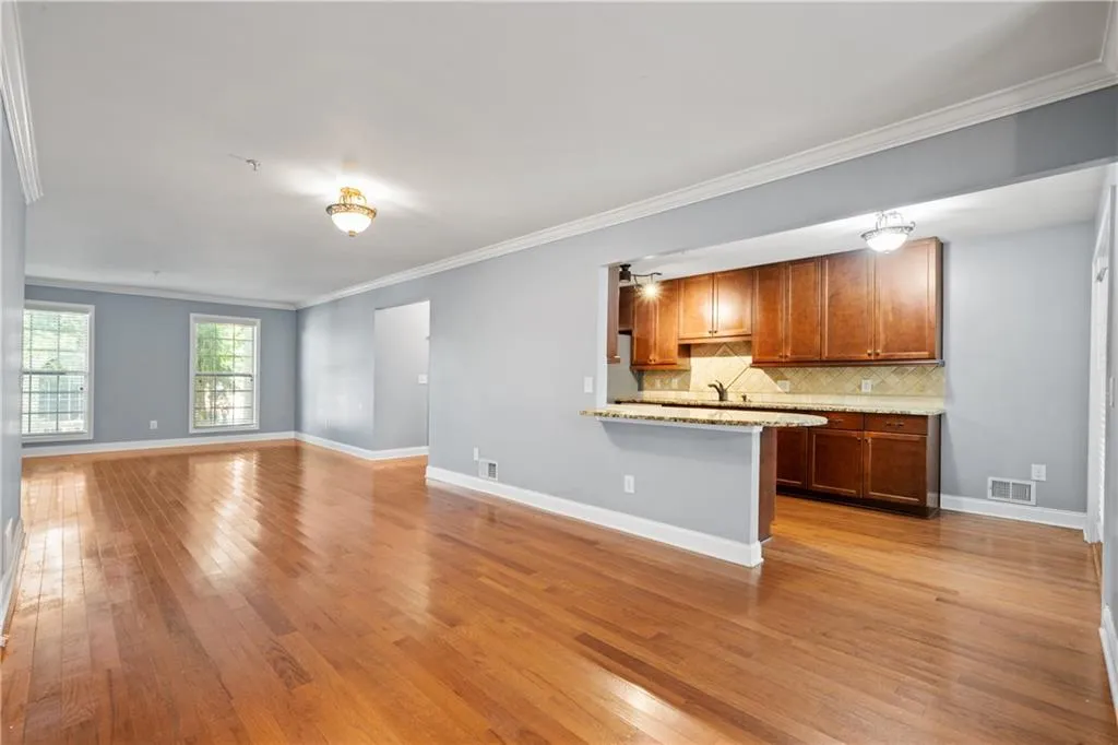 Kitchen featuring light hardwood / wood-style flooring, light stone countertops, kitchen peninsula, tasteful backsplash, and ornamental molding