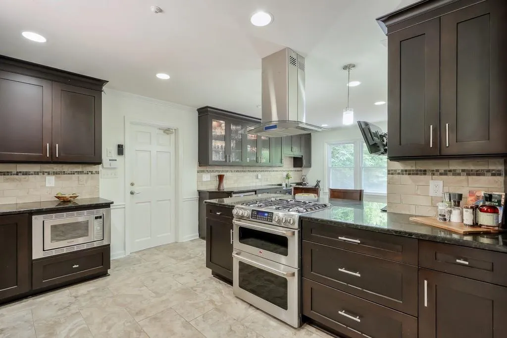 Kitchen featuring granite counters, range with two ovens, tasteful backsplash, white microwave, and a range hood