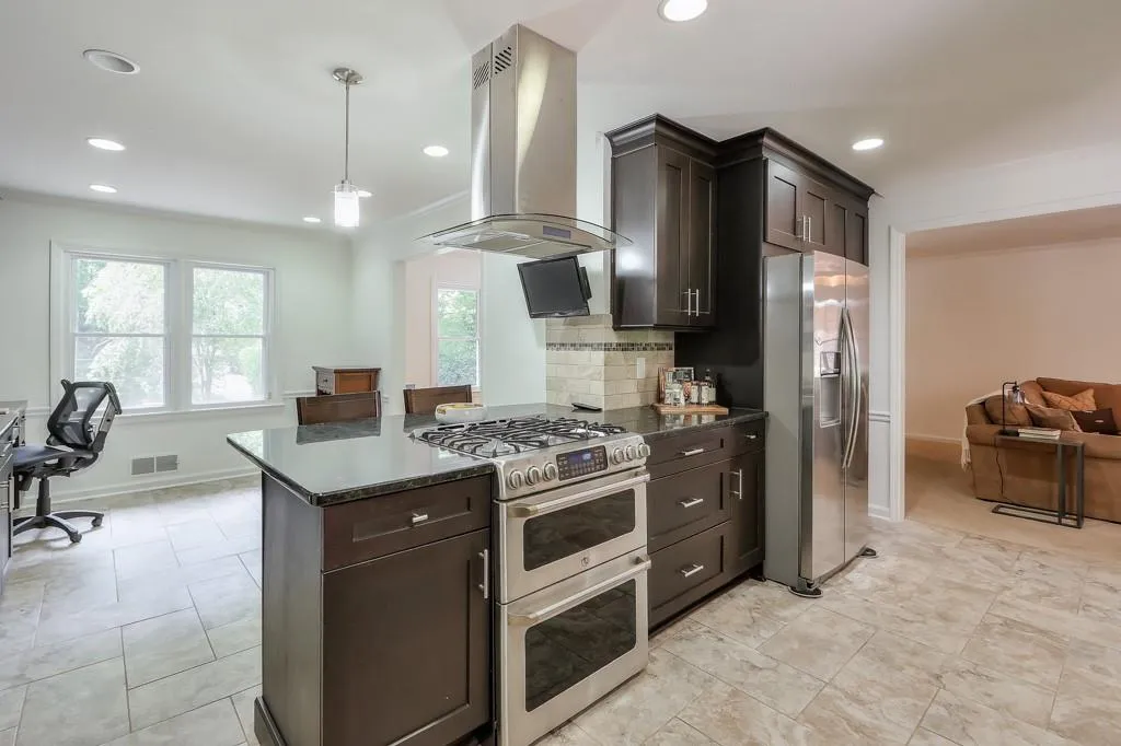 Kitchen with stainless steel appliances, a range hood, dark brown cabinets, and granite countertops
