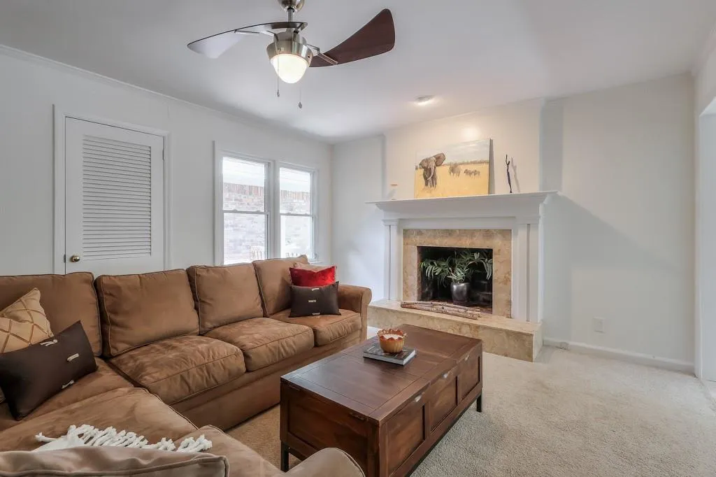 Living room with crown molding, light colored carpet, a fireplace, and ceiling fan
