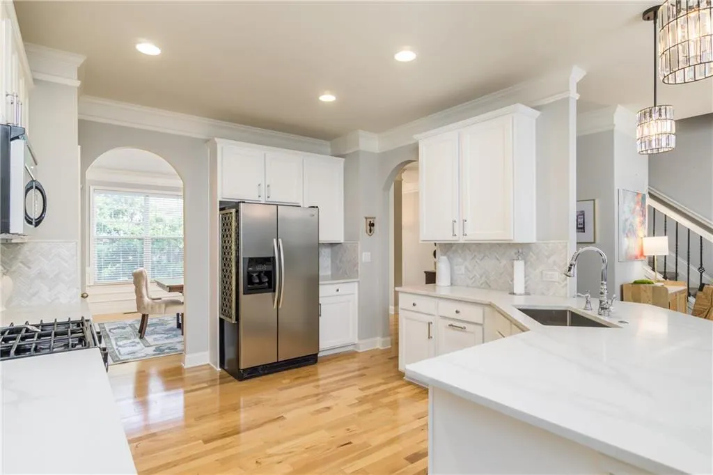 Kitchen featuring decorative backsplash, arched walkways, appliances with stainless steel finishes, ornamental molding, and white cabinets