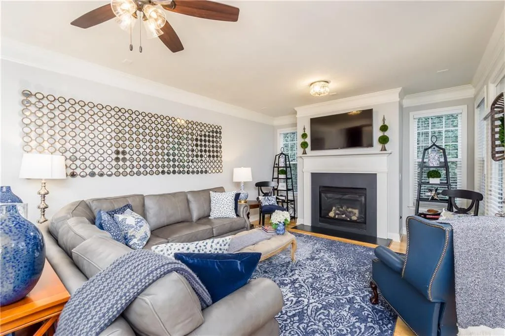 Living room with ornamental molding, a glass covered fireplace, wood finished floors, and a ceiling fan