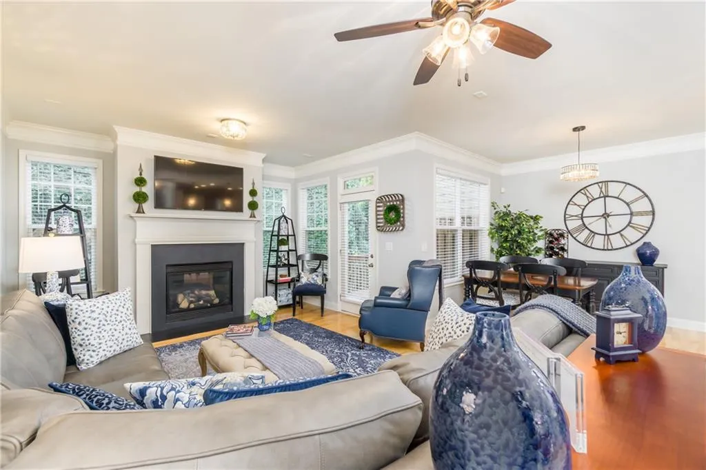 Living area with wood finished floors, plenty of natural light, crown molding, a glass covered fireplace, and a ceiling fan
