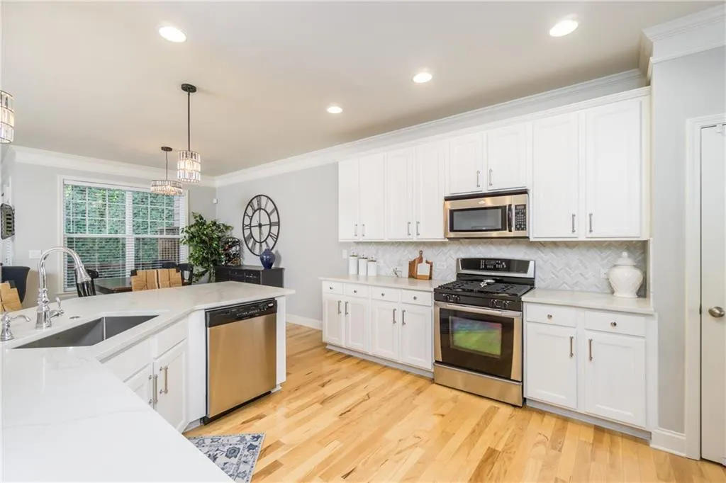 Kitchen with appliances with stainless steel finishes, crown molding, hanging light fixtures, white cabinetry, and light wood-style floors