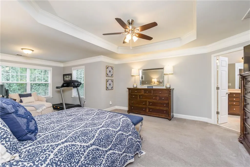 Bedroom featuring a raised ceiling, ornamental molding, light colored carpet, and a ceiling fan