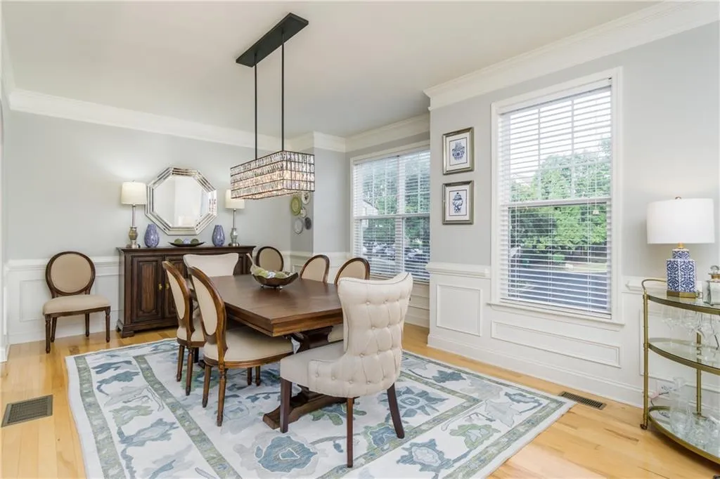 Dining area featuring a wainscoted wall, crown molding, a decorative wall, and light wood-style flooring