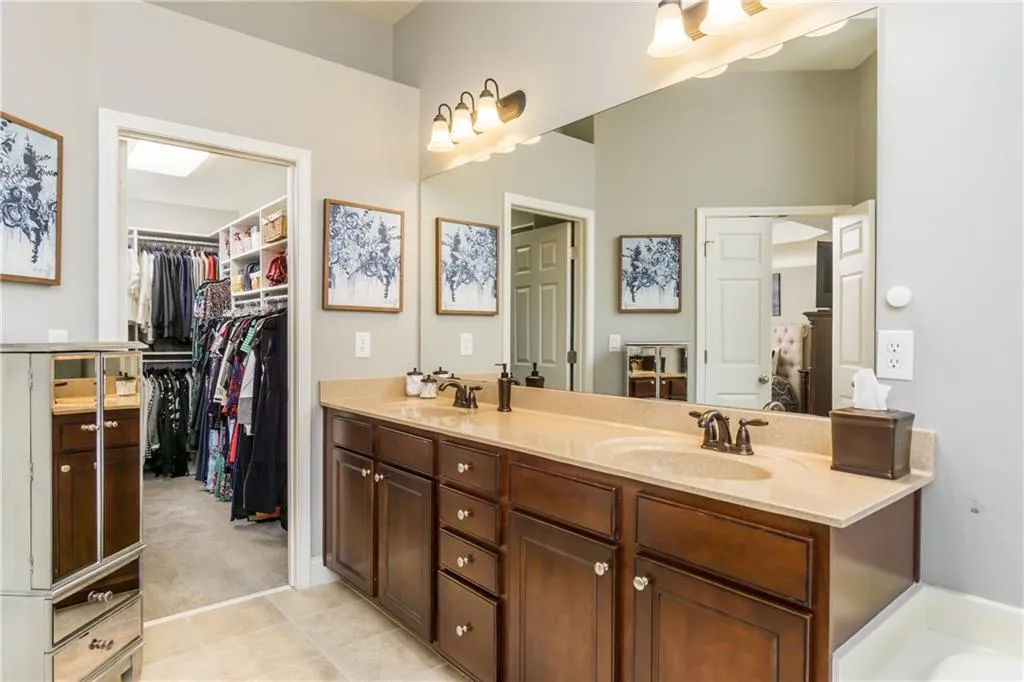 Full bathroom featuring double vanity, light colored carpet, light tile patterned floors, and a walk in closet