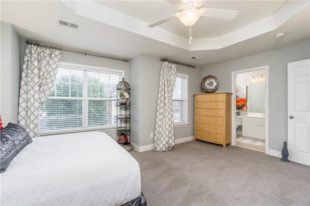 Bedroom featuring a tray ceiling, carpet floors, ceiling fan, and ensuite bathroom