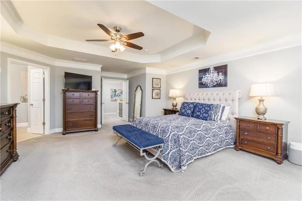 Bedroom with a raised ceiling, ornamental molding, carpet flooring, and a ceiling fan
