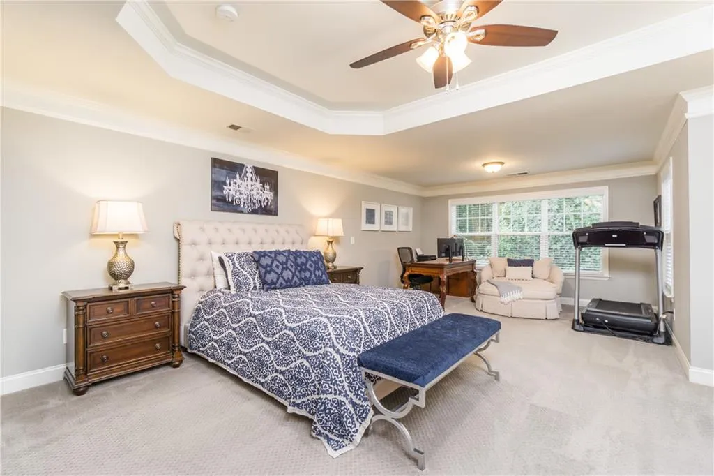 Bedroom featuring crown molding, light carpet, a tray ceiling, and ceiling fan
