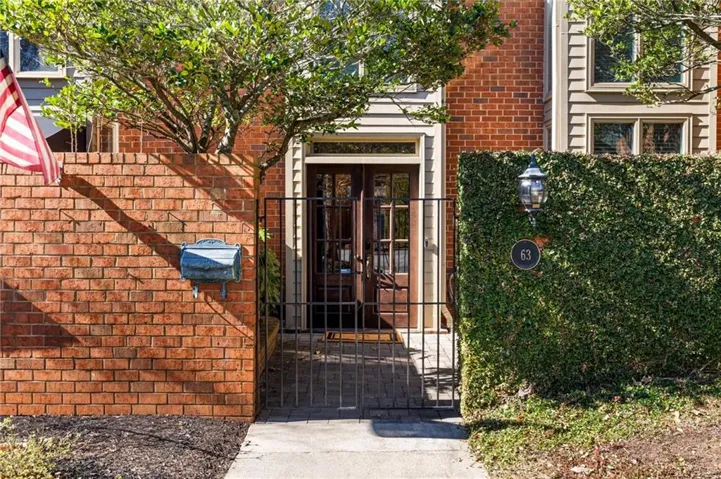 Brick facade, double entry doors, wrought iron gate, manicured hedge, and exterior wall lantern