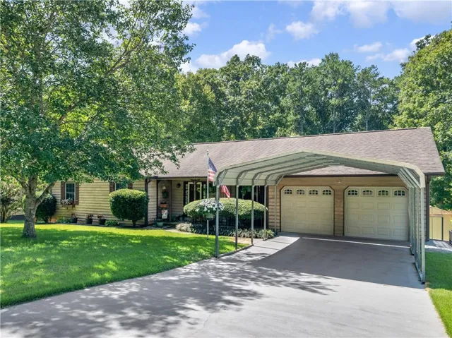 Charming ranch home featuring a two-car garage with paneled doors, welcoming front entrance with sidelights, and mature landscaping with established trees and manicured lawn