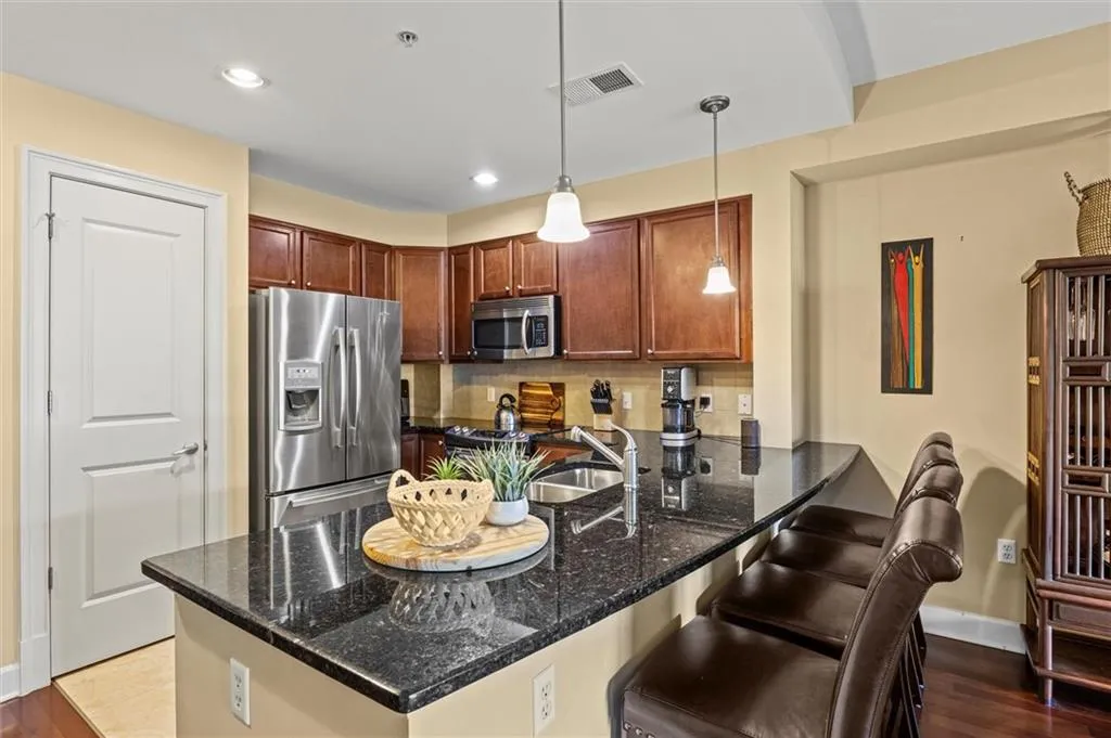 Kitchen with a kitchen breakfast bar, decorative light fixtures, appliances with stainless steel finishes, kitchen peninsula, and dark stone counters