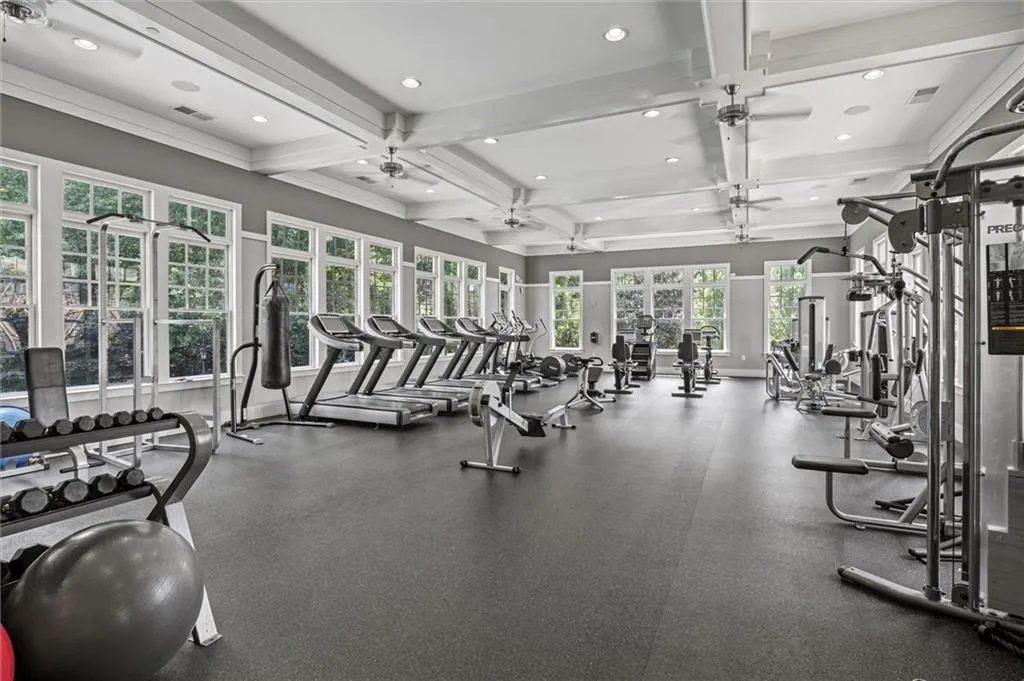 Gym with coffered ceiling, a wealth of natural light, and ceiling fan