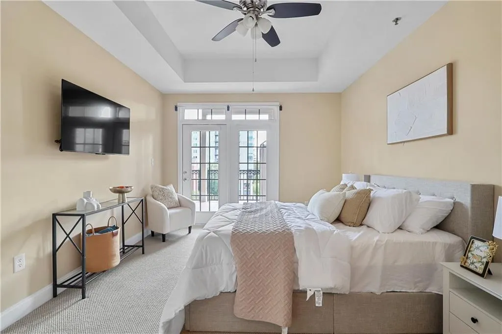 Carpeted bedroom featuring a raised ceiling, access to exterior, and a ceiling fan