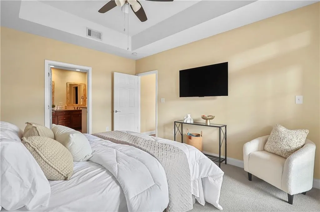 Bedroom featuring carpet flooring, connected bathroom, a tray ceiling, and a ceiling fan