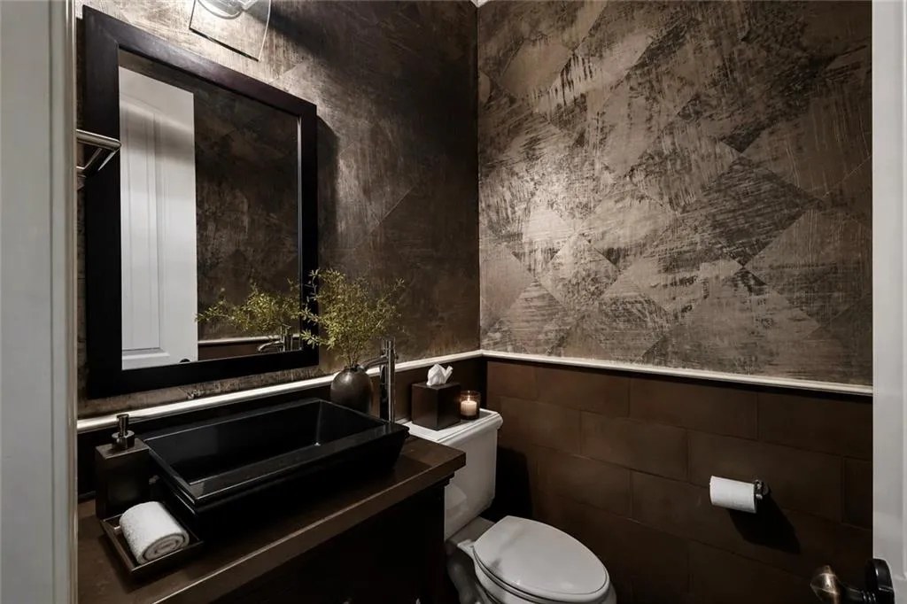 Powder room featuring a vessel sink, dark wood-finish vanity, framed mirror, and textured wall covering