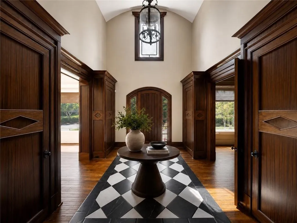 Grand foyer featuring dark wood paneling, arched ceilings, a striking checkered floor inlay, wood-finish flooring, and an elegant overhead lantern fixture