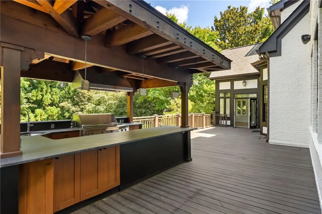 Expansive outdoor deck featuring a covered cooking station, built-in stainless steel grill, integrated range hood, ample counter space, and wood-finish cabinetry