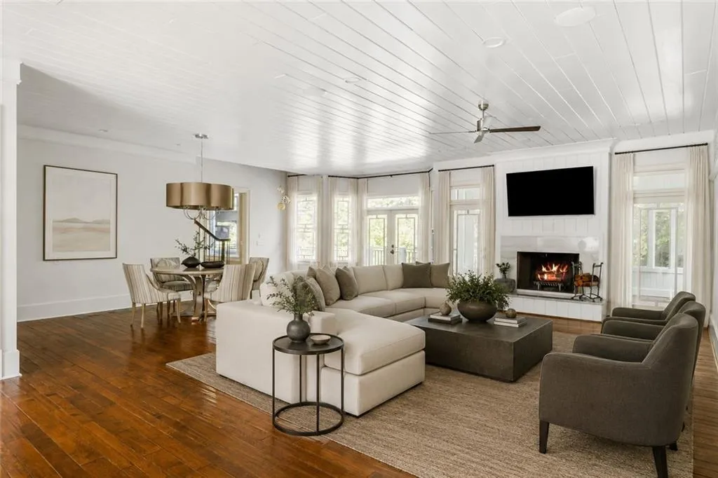Expansive open-concept space featuring rich wood-finish flooring, a white paneled ceiling, and a fireplace with a stone surround
