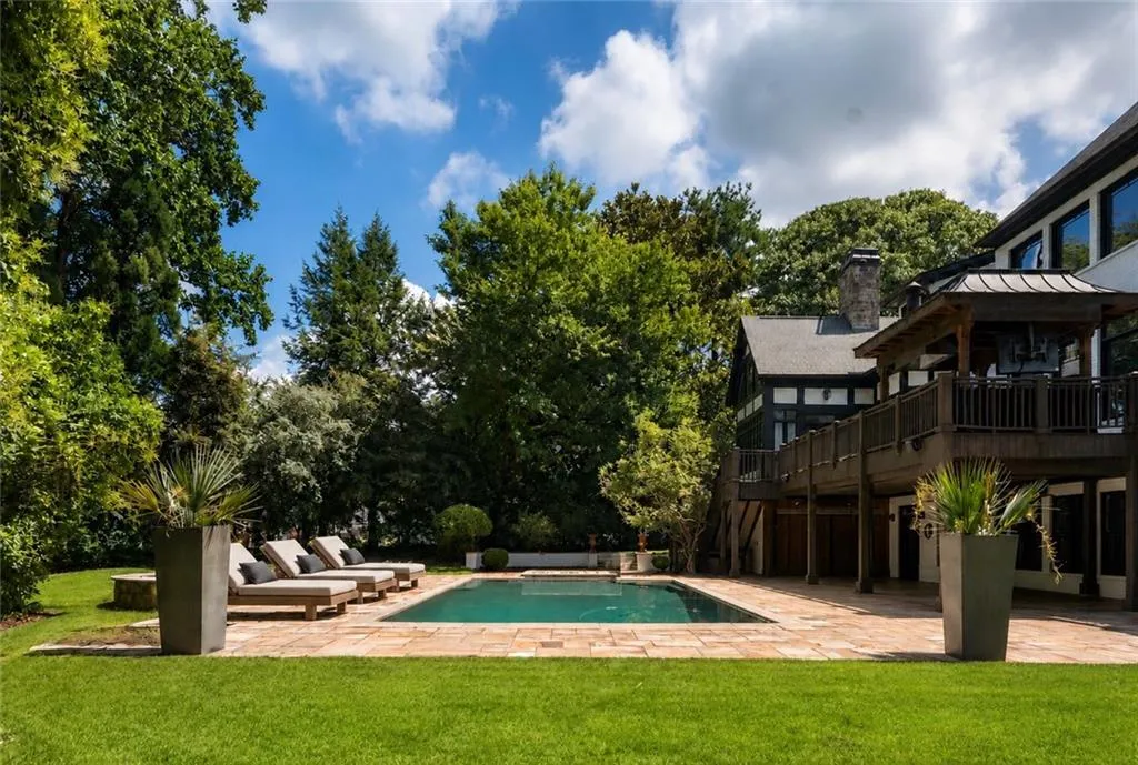 In-ground pool with surrounding paver patio, expansive lawn, mature tree landscaping, and a multi-level deck with a covered gazebo