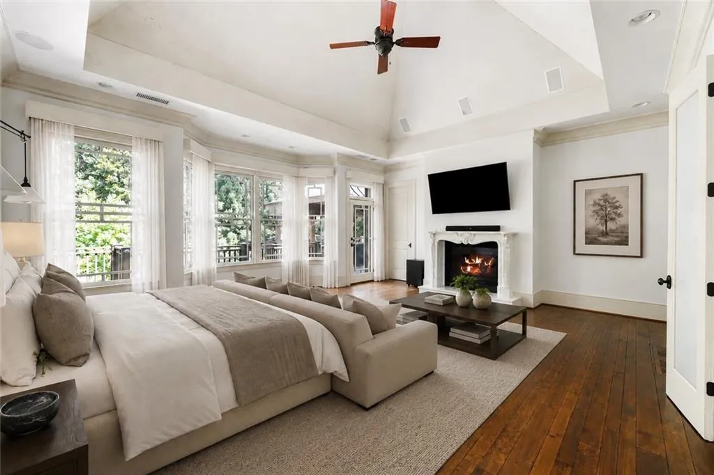 Vaulted ceiling with a ceiling fan, hardwood flooring, fireplace with a decorative mantel, multiple windows, and a glass-paneled door