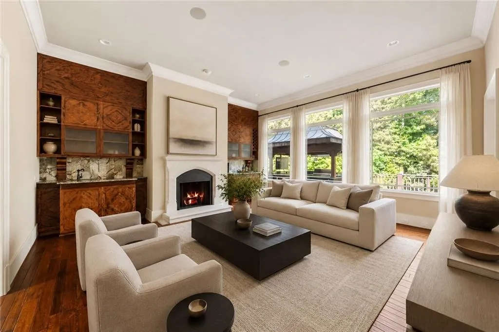 Hardwood flooring, a built-in wet bar with cabinetry, a stone-surround fireplace, large windows with exterior access, and recessed lighting