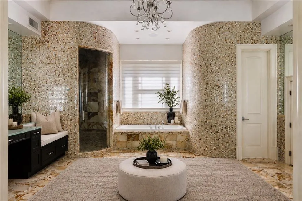 Mosaic tile walls, built-in soaking tub, glass-enclosed shower, custom vanity with integrated seating, and stone-finish flooring