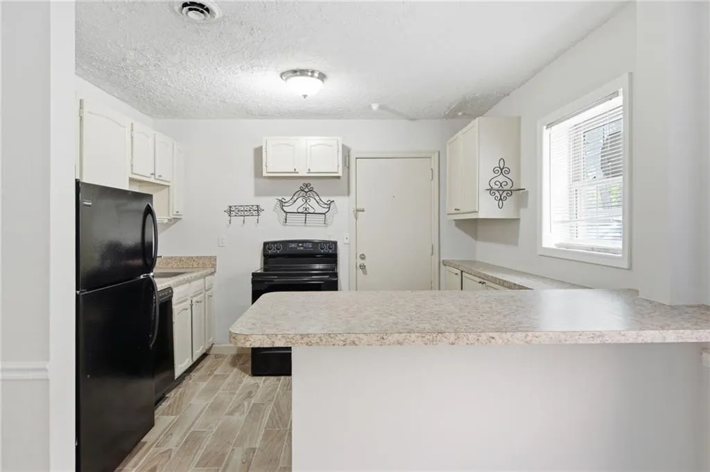 Kitchen featuring wood-finish flooring, white cabinetry, black appliances, light-toned countertops, and a breakfast bar