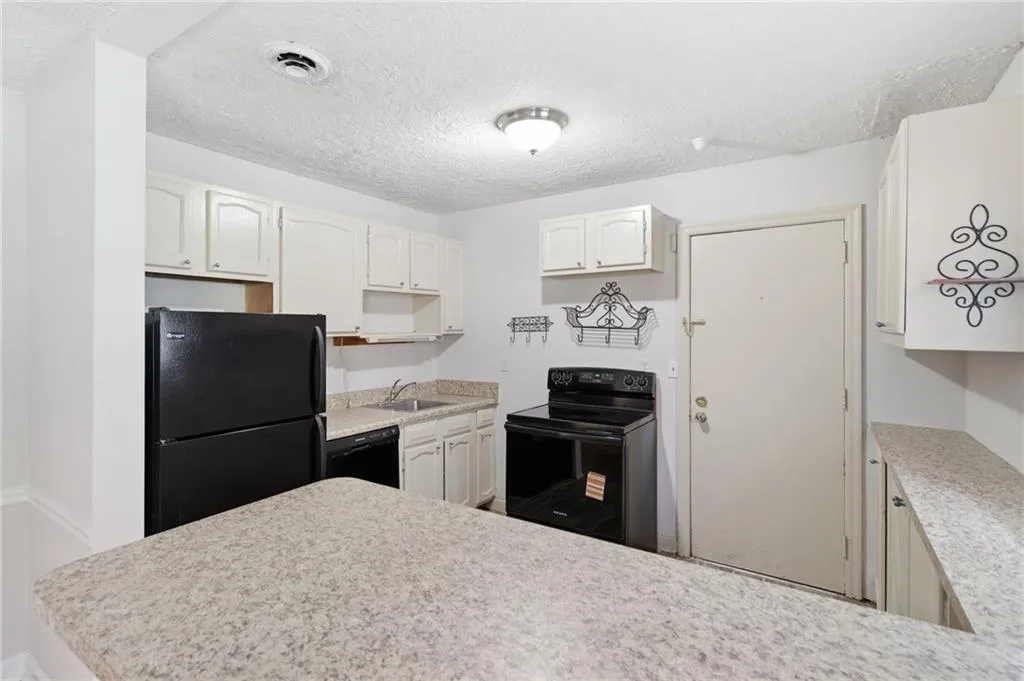 Kitchen featuring white cabinetry, speckled countertops, black appliances, and a built-in sink