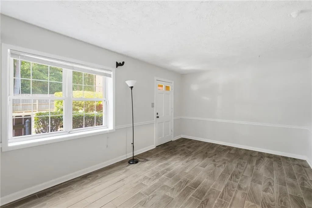 Spacious room with wood-finish flooring, large window, and light gray walls featuring chair rail molding