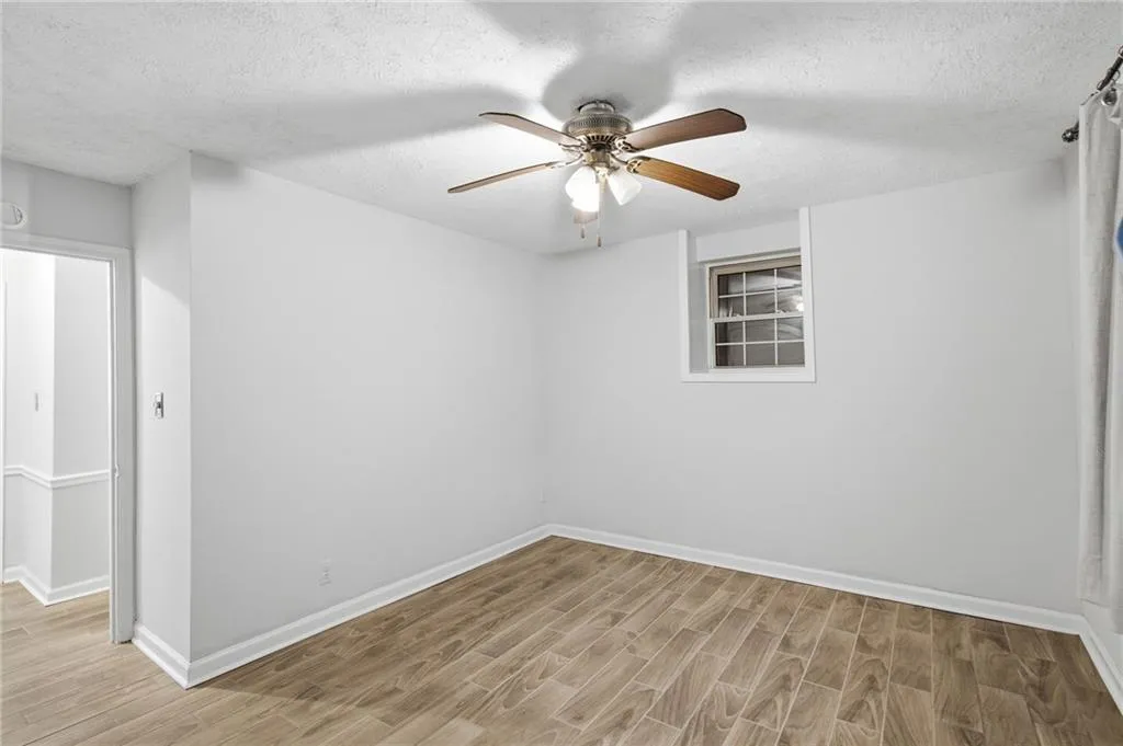 Wood-finish flooring, ceiling fan with light fixture, single window, and white painted walls