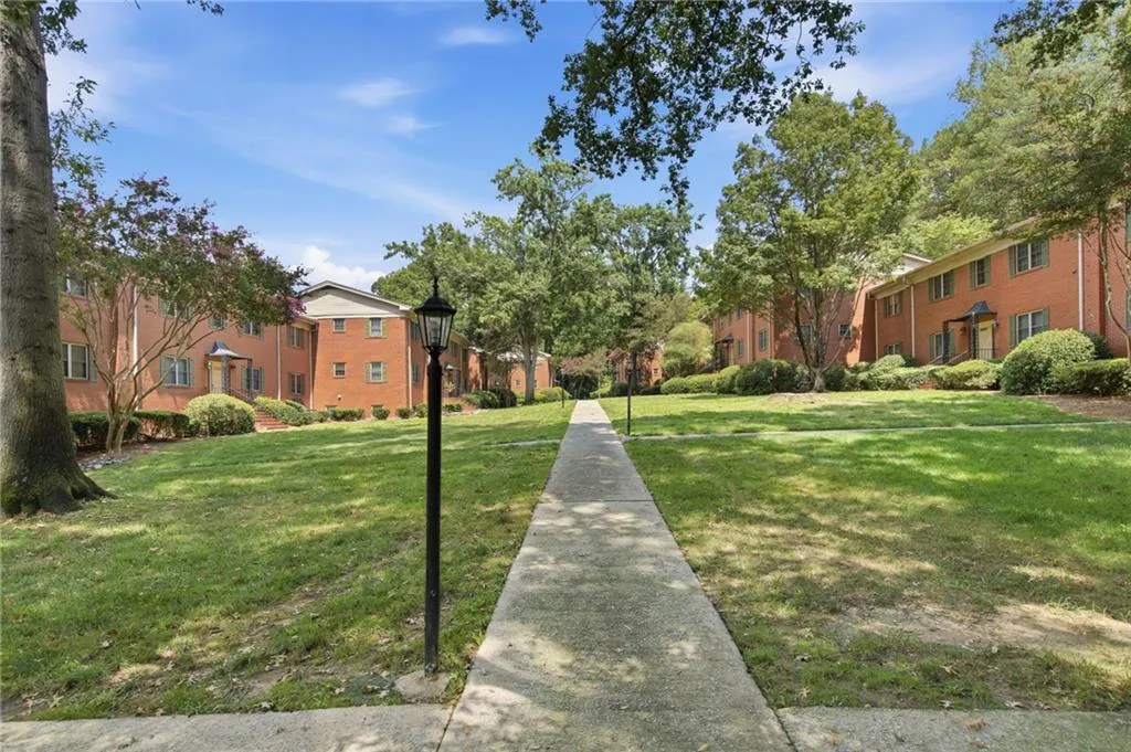 Expansive green space featuring a concrete walkway, mature trees, and landscaping, with brick-faced residential buildings