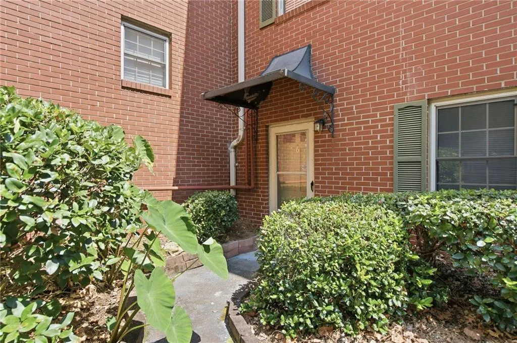 Red brick exterior with a black metal awning, green louvered shutters, and established landscaping