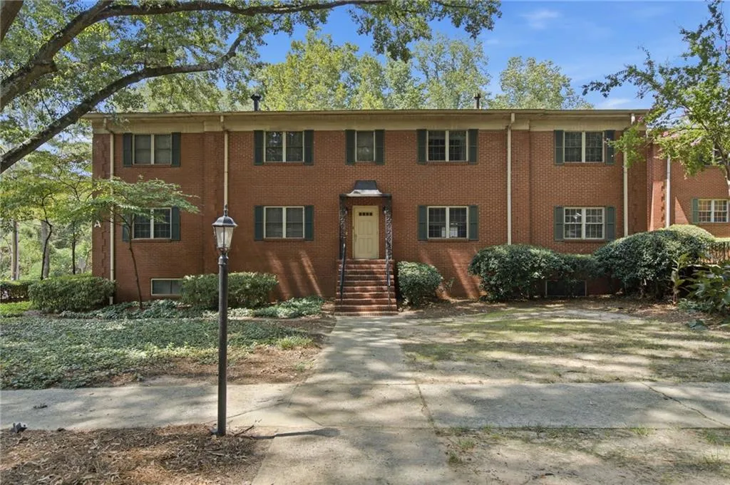 Brick exterior with green shutter accents, concrete pathway, established landscaping, and a streetlamp