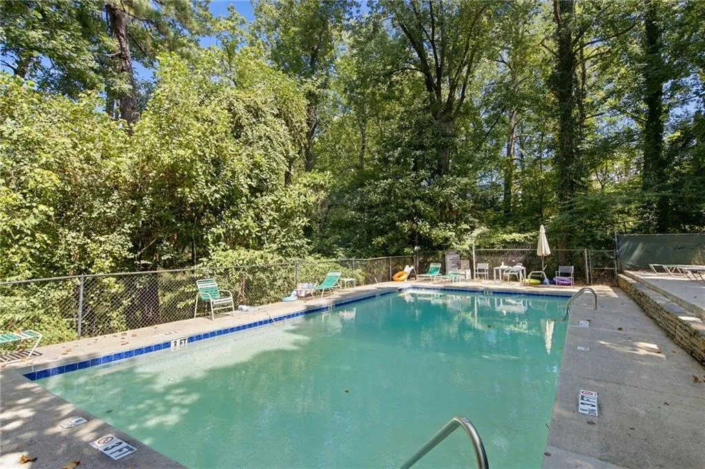 Rectangular swimming pool with metal handrails, surrounded by a concrete deck and lush tree canopy