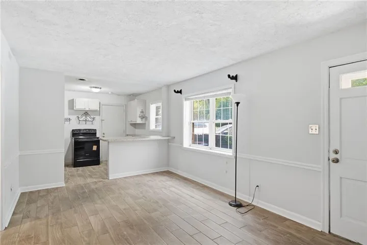 Bright and open living space featuring wood-finish flooring throughout, white shaker-style cabinetry with ample storage, stainless steel appliances, and abundant natural light from multi-pane windows