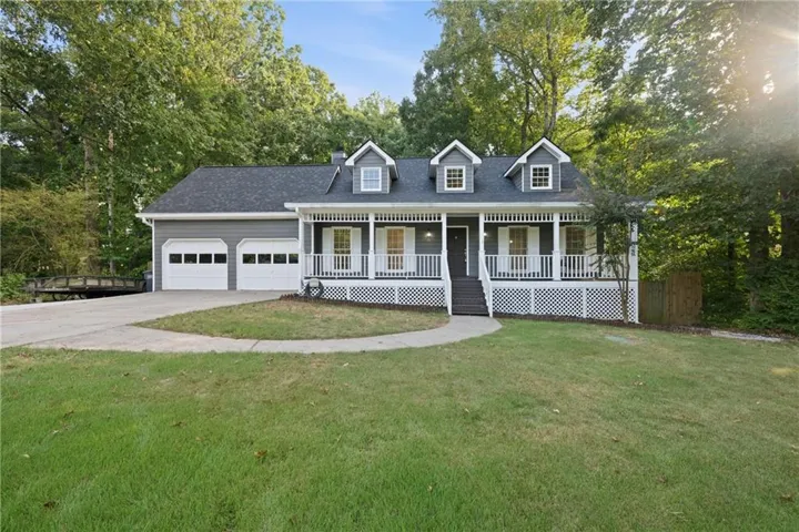 Exterior featuring gray siding, a covered front porch with white railings, a two-car garage, and a circular driveway
