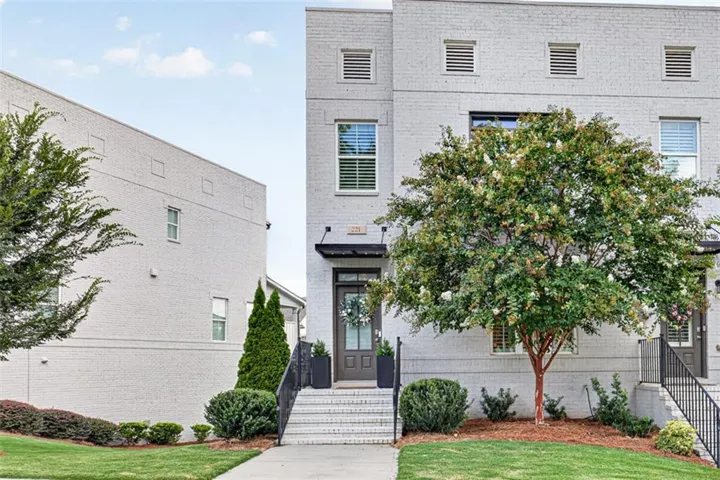 Modern townhouse exterior featuring light-colored brick, a dark front door with transom window, and a black awning