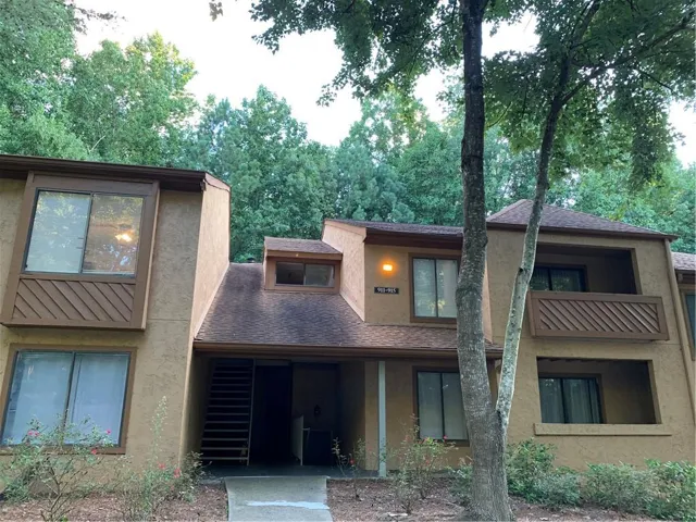 Multi-story stucco exterior featuring multiple windows and a brown shingle roof