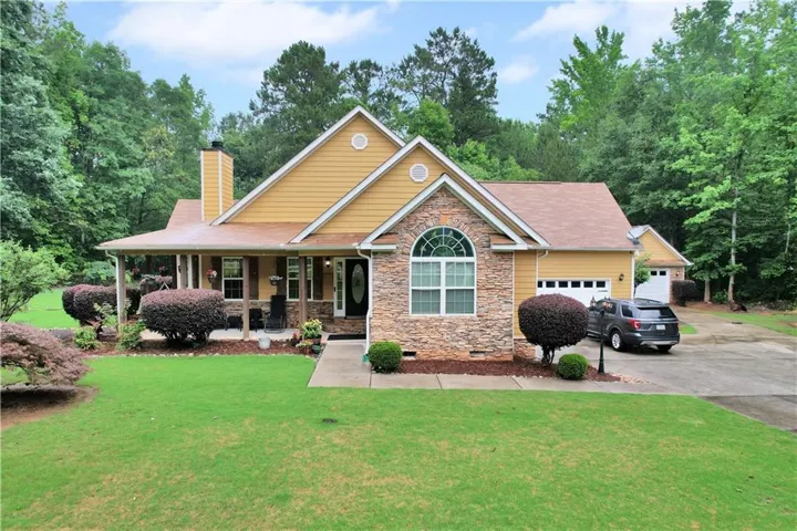 Yellow siding exterior with stone accents, covered front porch, arched window, attached garage, and detached garage